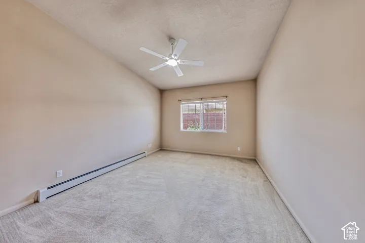Carpeted interior space featuring a window with blinds, a ceiling fan, and baseboard heating