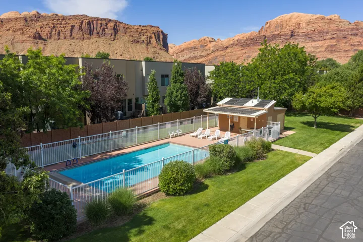 Fenced swimming pool area featuring a pool house with solar panels, surrounded by a manicured lawn and mature trees