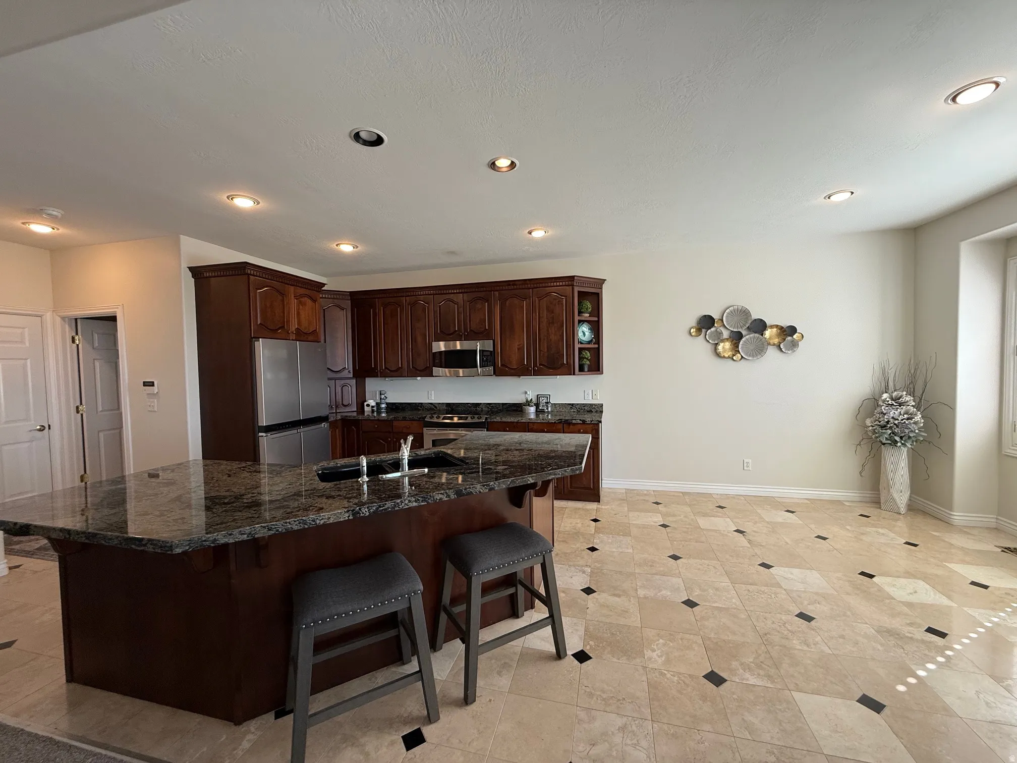 Spacious kitchen featuring dark wood cabinetry, stainless steel appliances, and a large island with a dark stone countertop and integrated sink