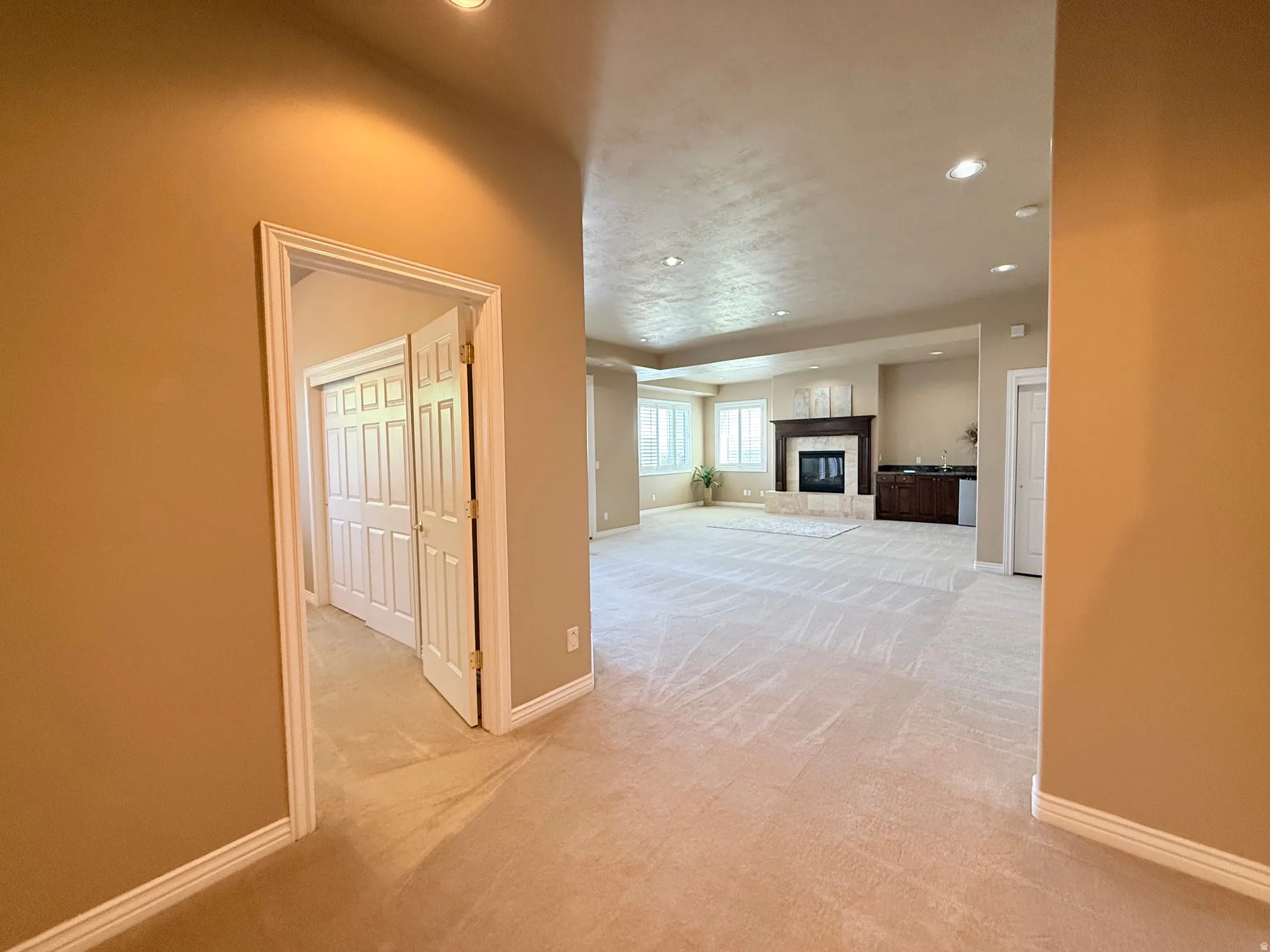 Spacious room with plush carpeting, recessed lighting, and a prominent fireplace featuring a dark wood mantel and light-toned stone surround