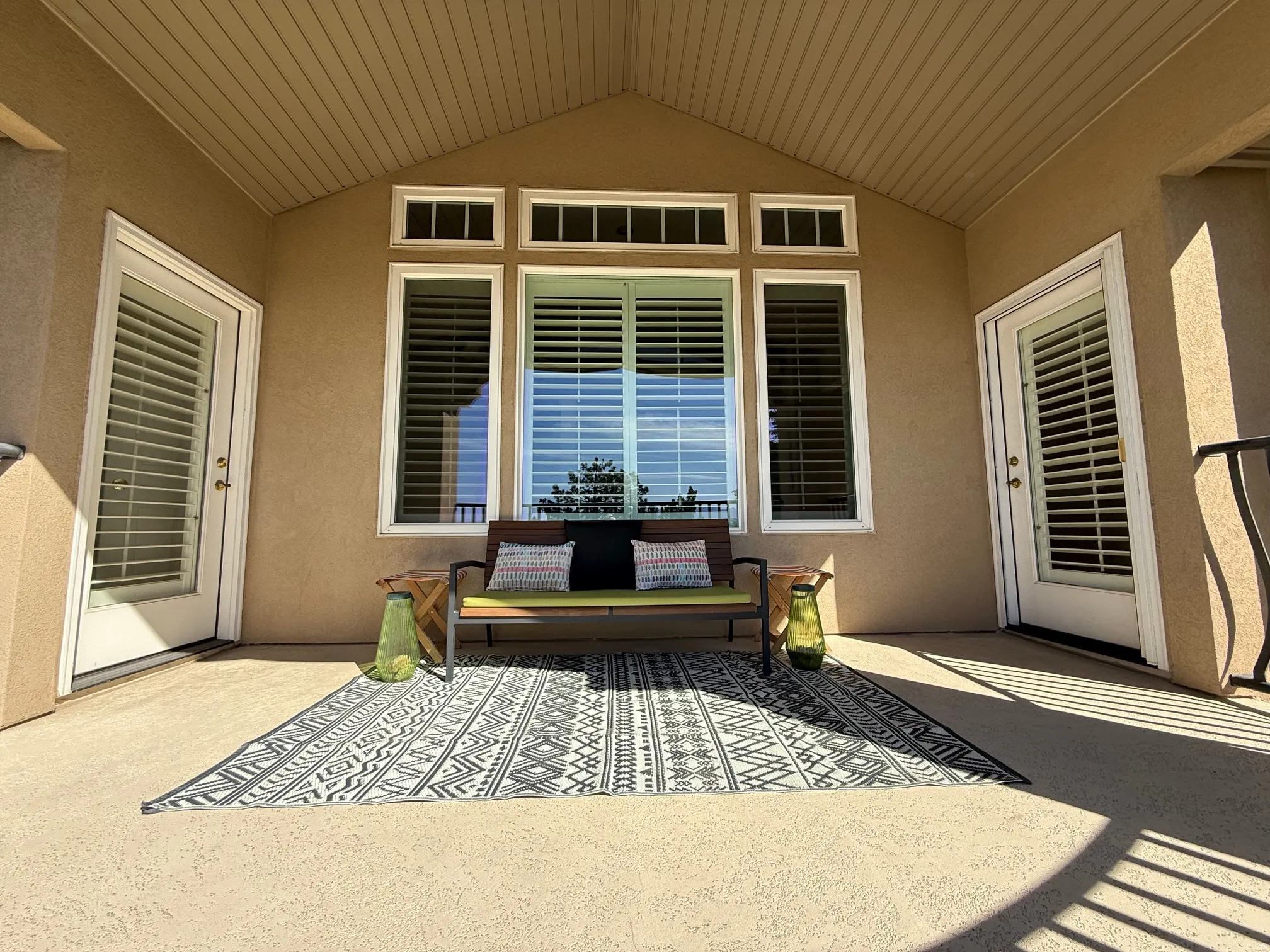 Covered patio featuring an angled wood-finish ceiling, textured exterior walls, multiple windows with plantation shutters, and two glass-paneled doors with internal blinds