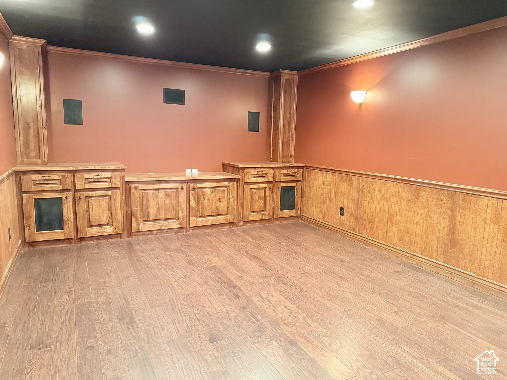 Wood-finish flooring with accent wall paneling, built-in cabinetry, recessed lighting, and wall sconces