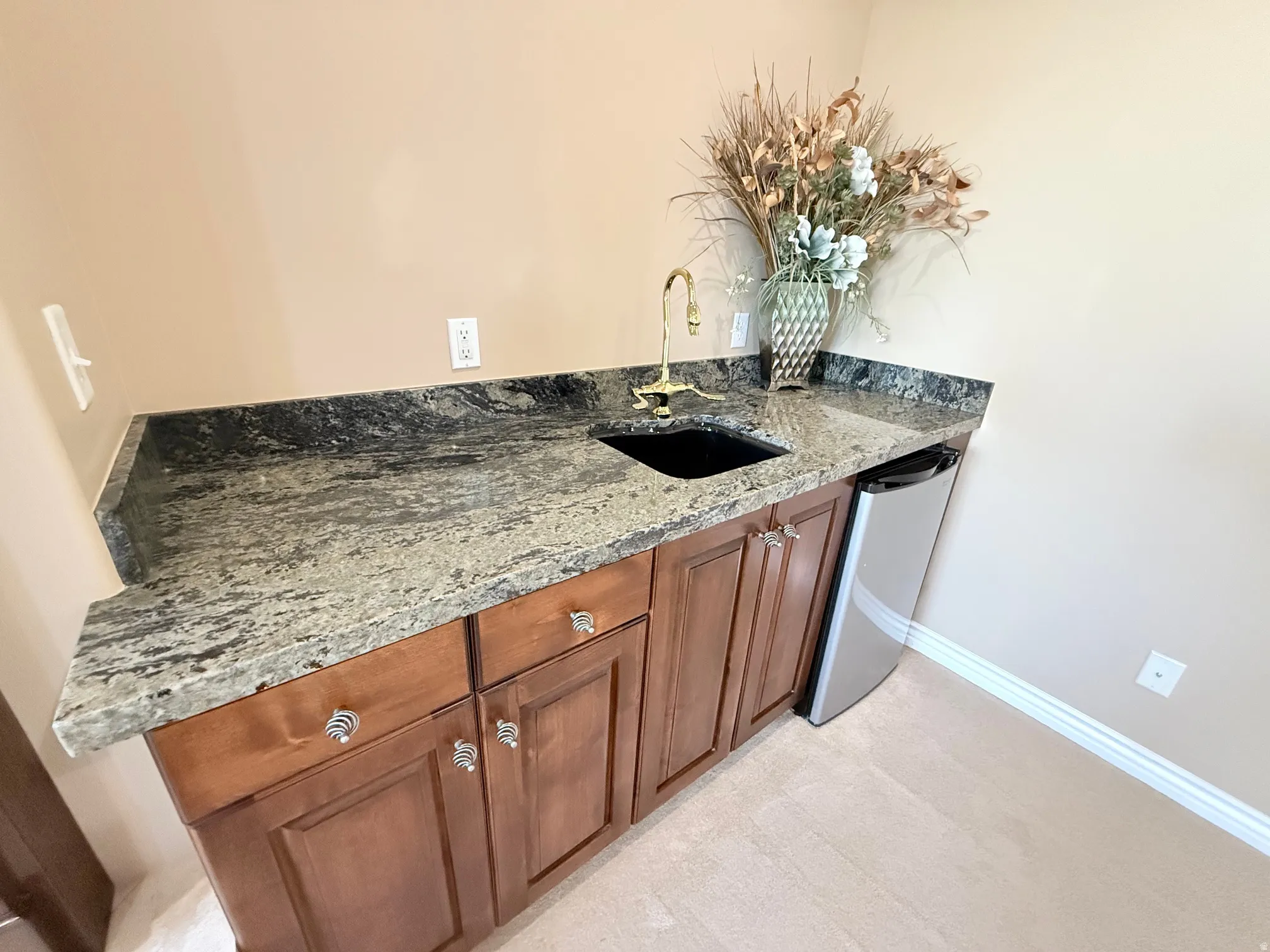Wet bar featuring a dark granite countertop with a polished finish, undermount sink, and a brass faucet