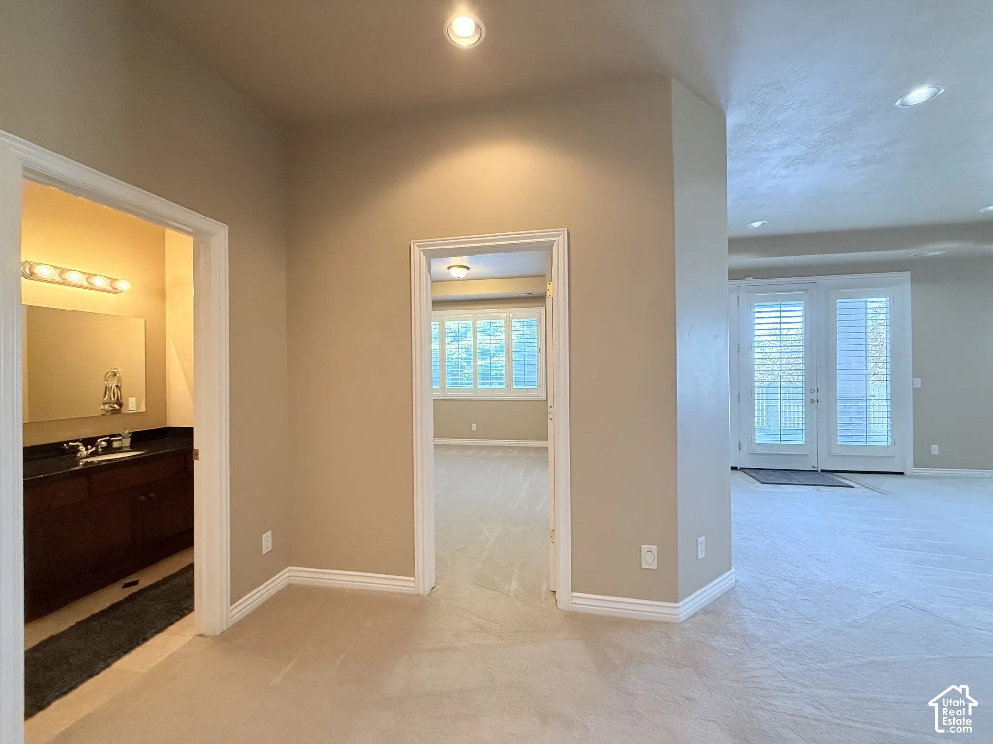 Plush carpeting throughout with recessed lighting, double doors with plantation shutters, and a full vanity with a dark countertop and ample storage