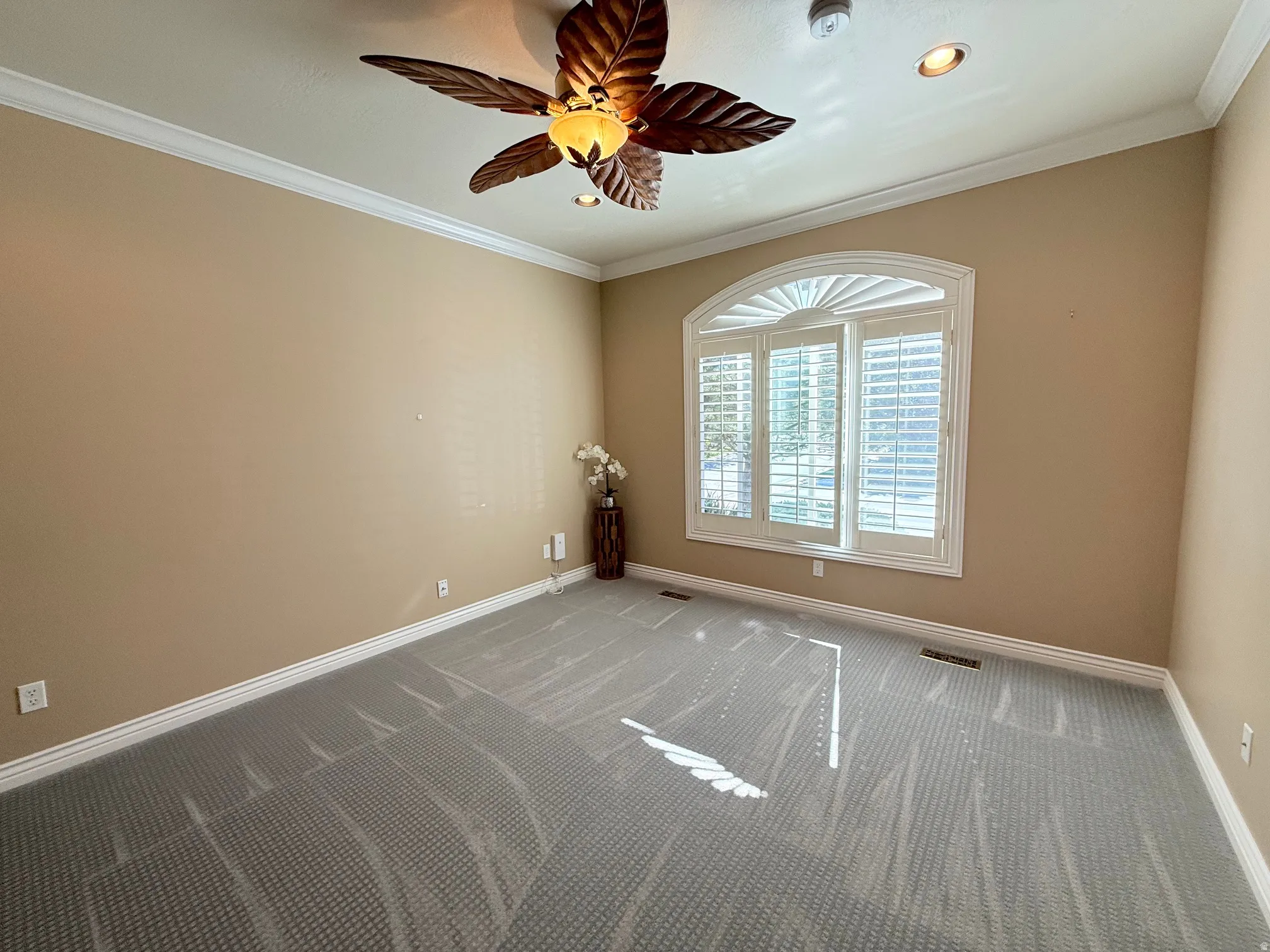Room featuring an arched window with plantation shutters, crown molding, and a decorative ceiling fan