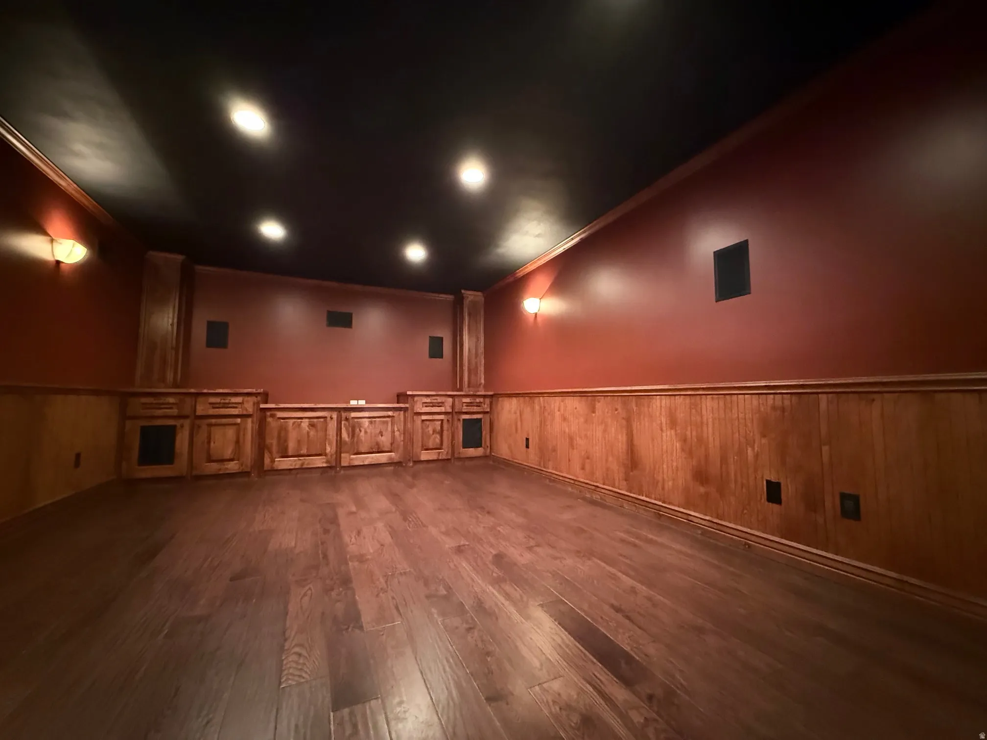 Theater room featuring dark wood-finish flooring, recessed ceiling lighting, and built-in cabinetry with integrated speakers