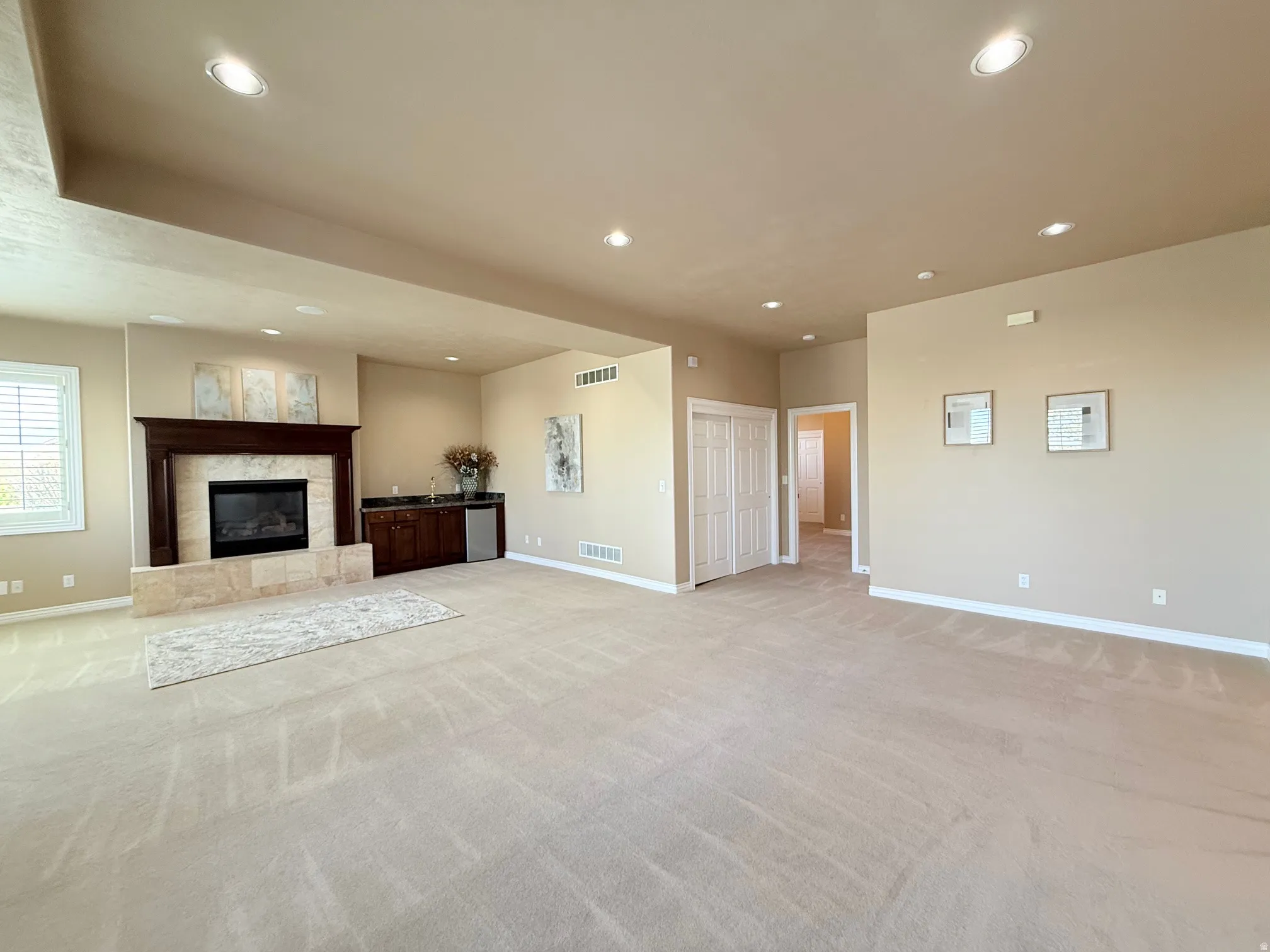 Spacious room featuring a fireplace with a wood mantle and stone surround, a built-in wet bar with cabinetry, recessed lighting, and neutral-toned carpeting