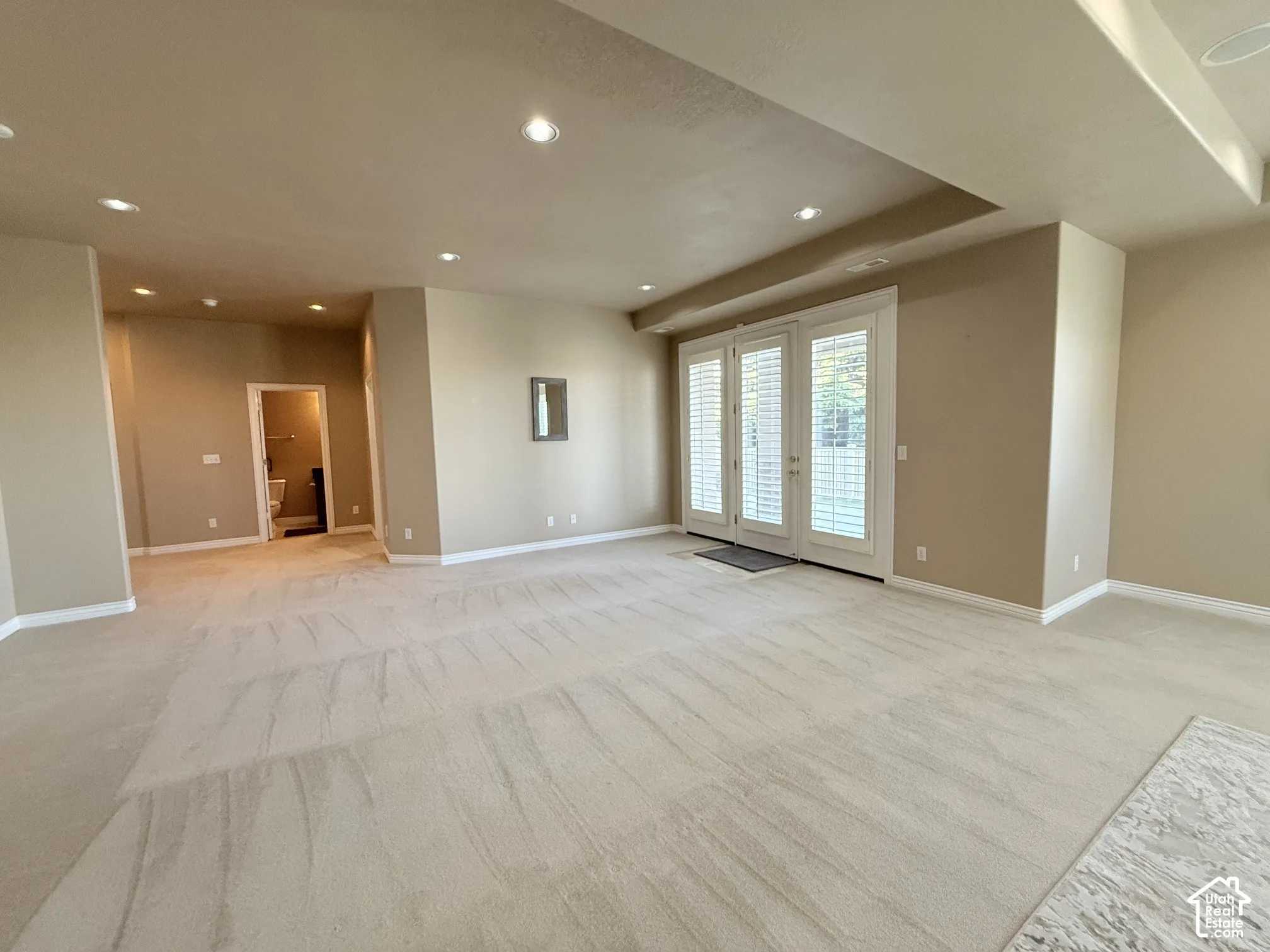 Spacious room featuring neutral carpeting, recessed ceiling lighting, and a tray ceiling detail