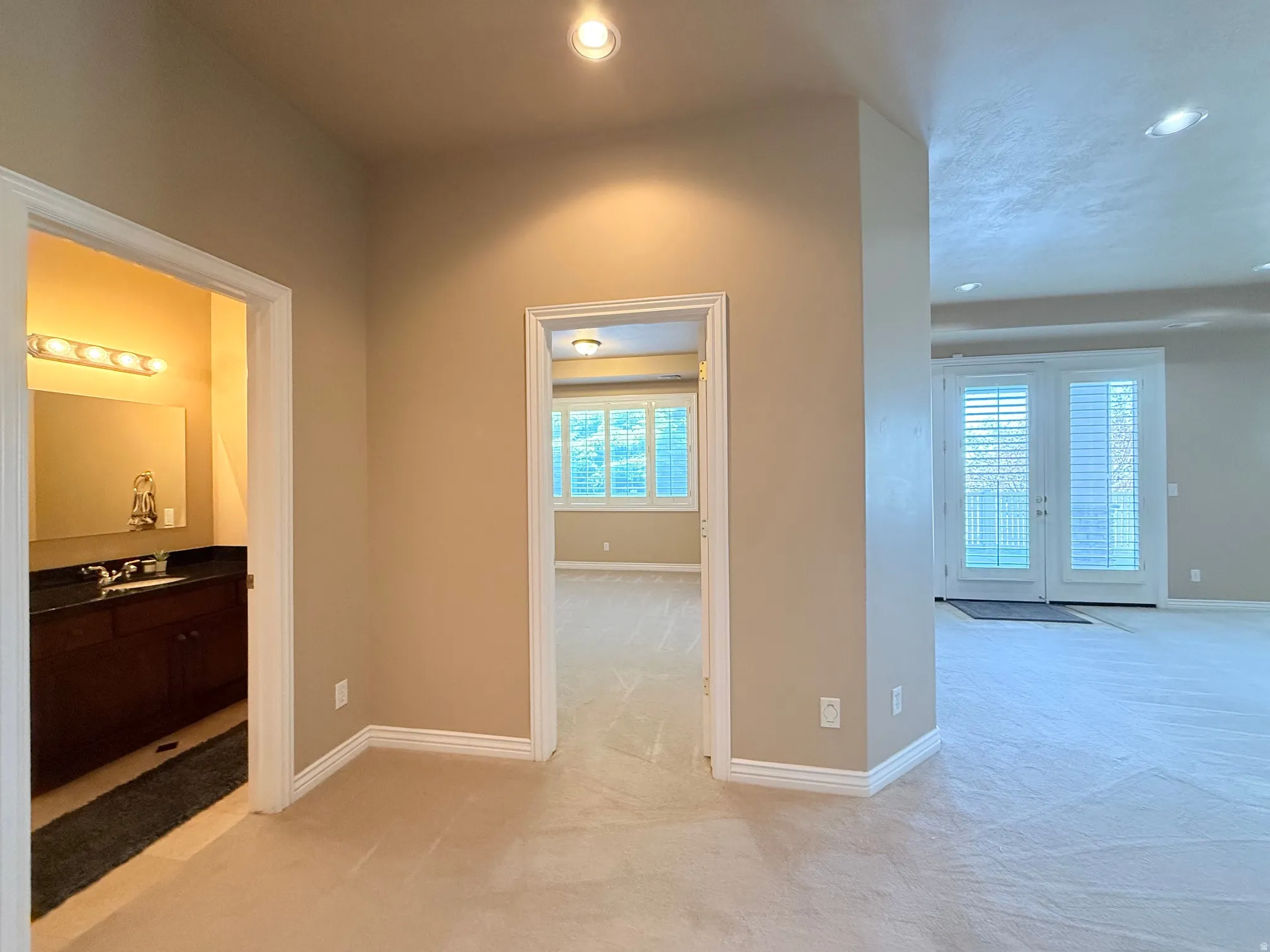 Plush carpeting throughout with recessed lighting, double doors with plantation shutters, and a full vanity with a dark countertop and ample storage