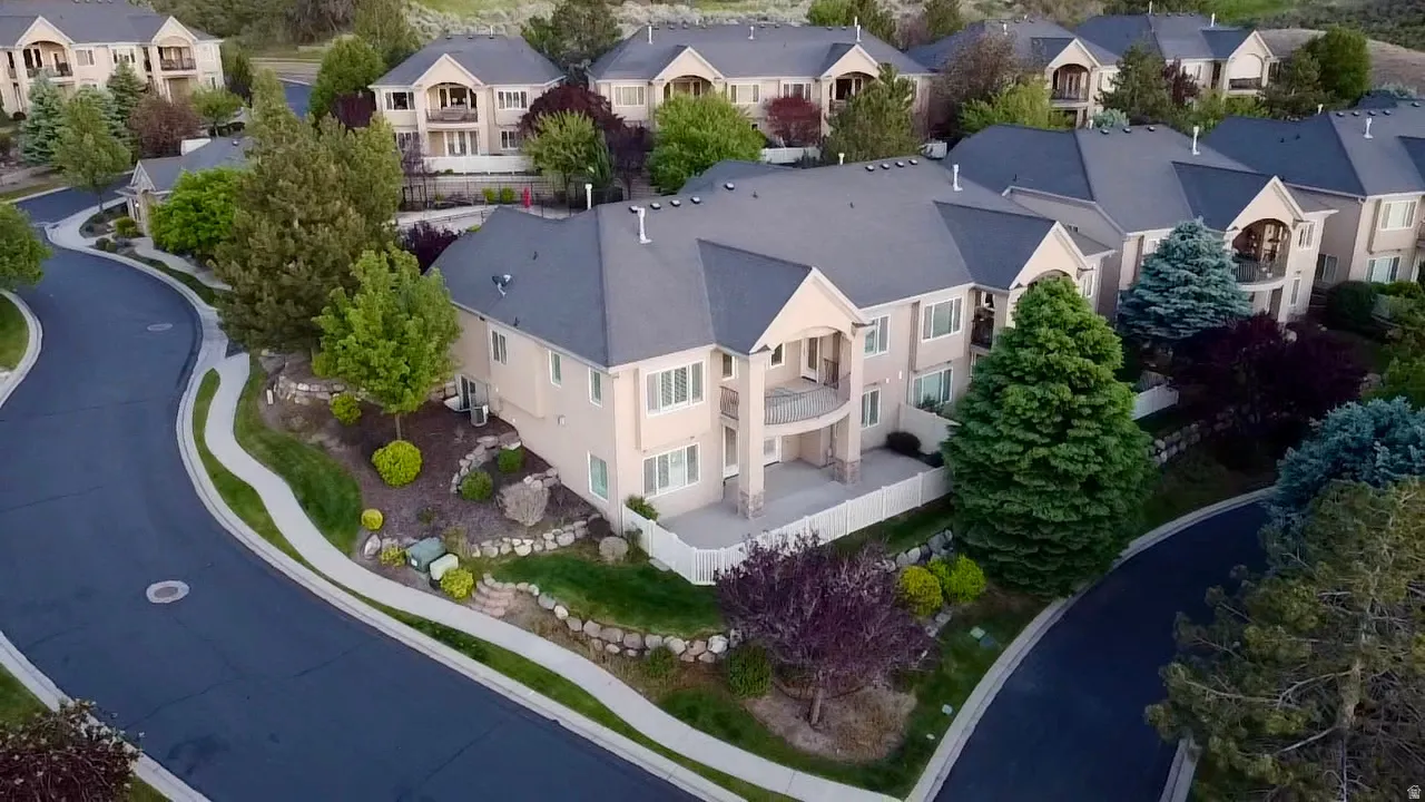 Stucco exterior residence with a dark gray shingle roof, featuring multiple balconies and mature landscaping
