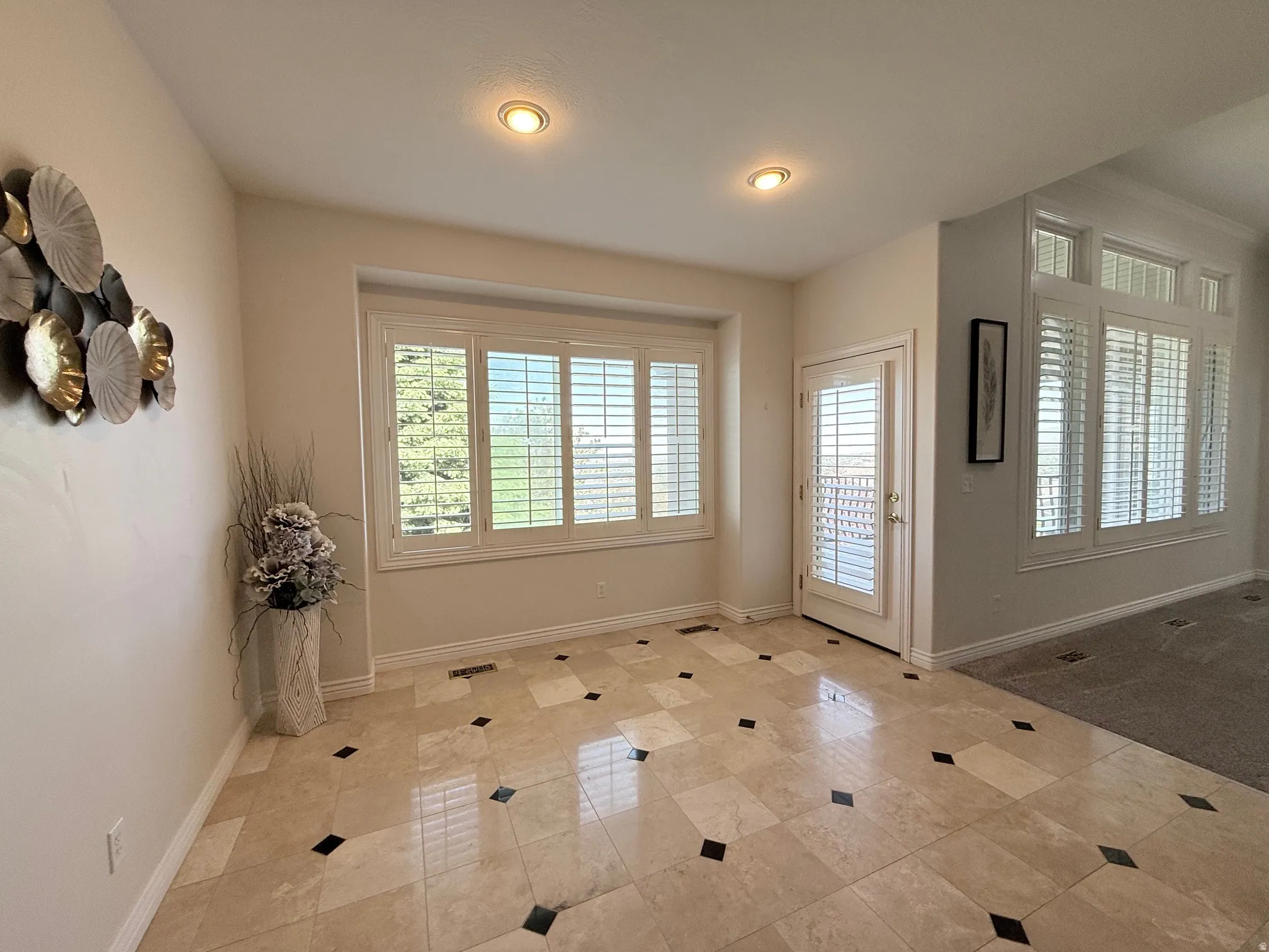 Tiled entryway featuring a decorative inlay pattern, recessed lighting, and white plantation shutters on the window and glass-paned door