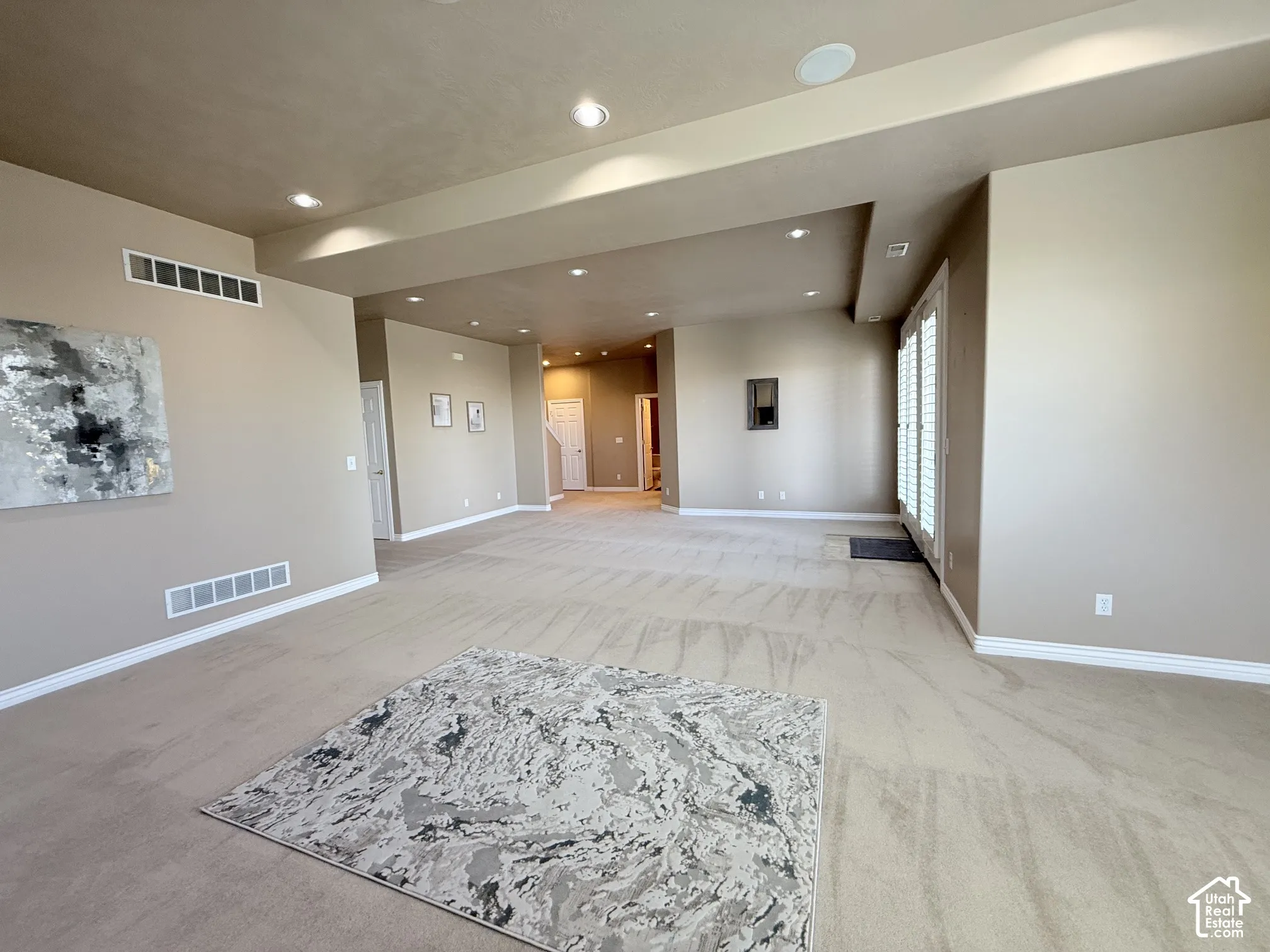Spacious interior room with neutral-toned walls, recessed lighting, and light-colored carpet flooring