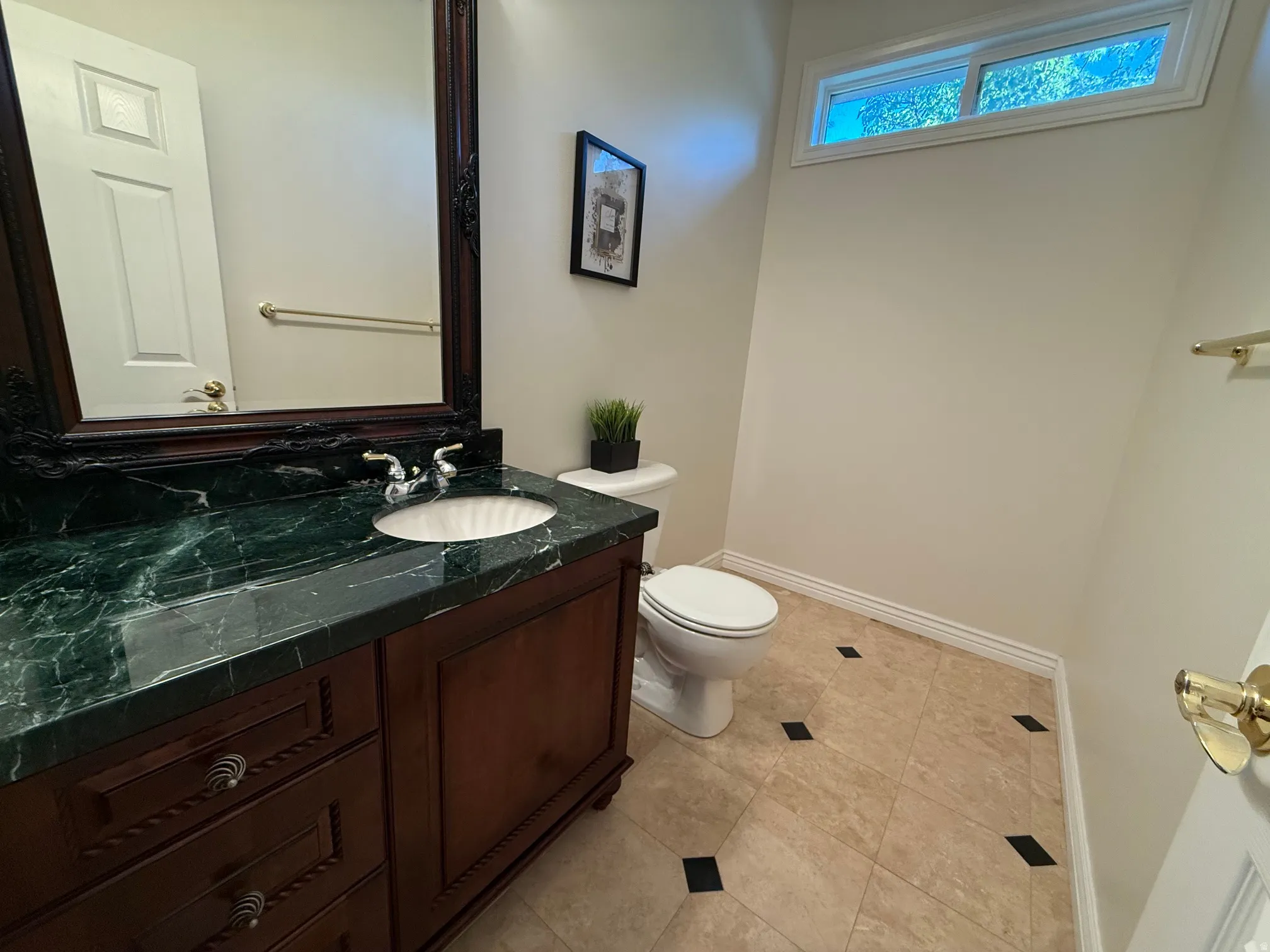 Bathroom vanity featuring a dark wood cabinet with decorative drawer pulls, a green marbled countertop, and an undermount sink with chrome fixtures