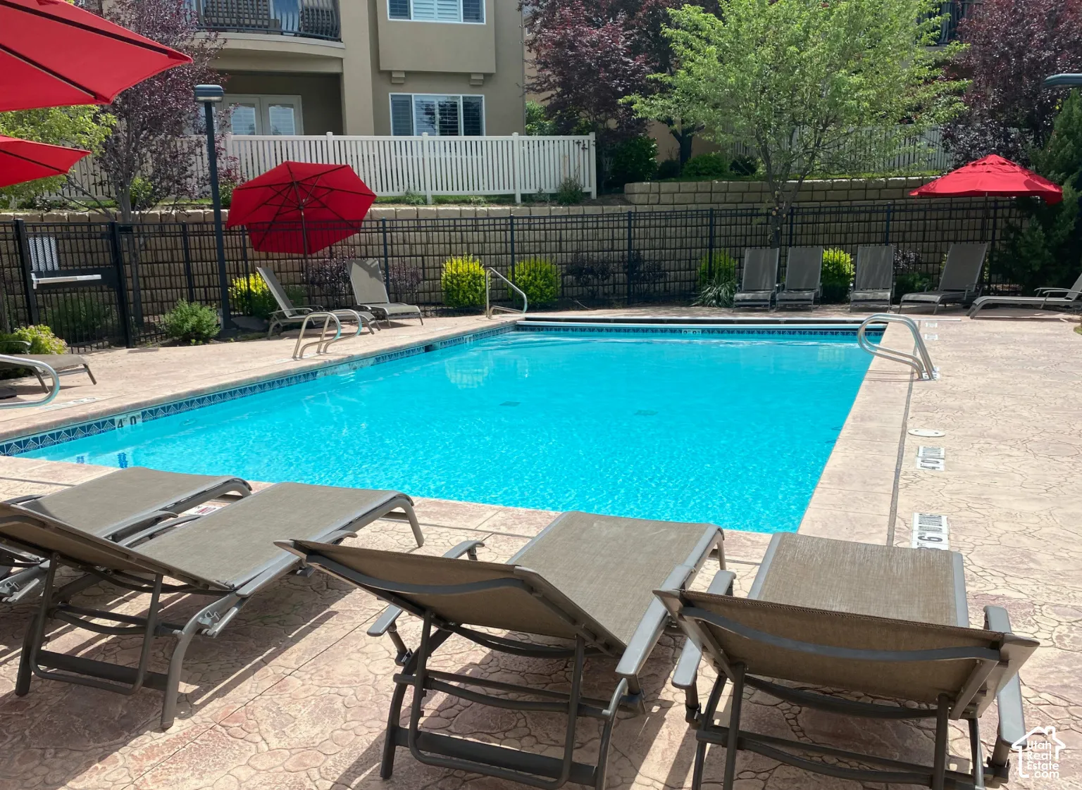 Refreshing swimming pool featuring a patterned concrete deck, perimeter fencing, and mature landscaping