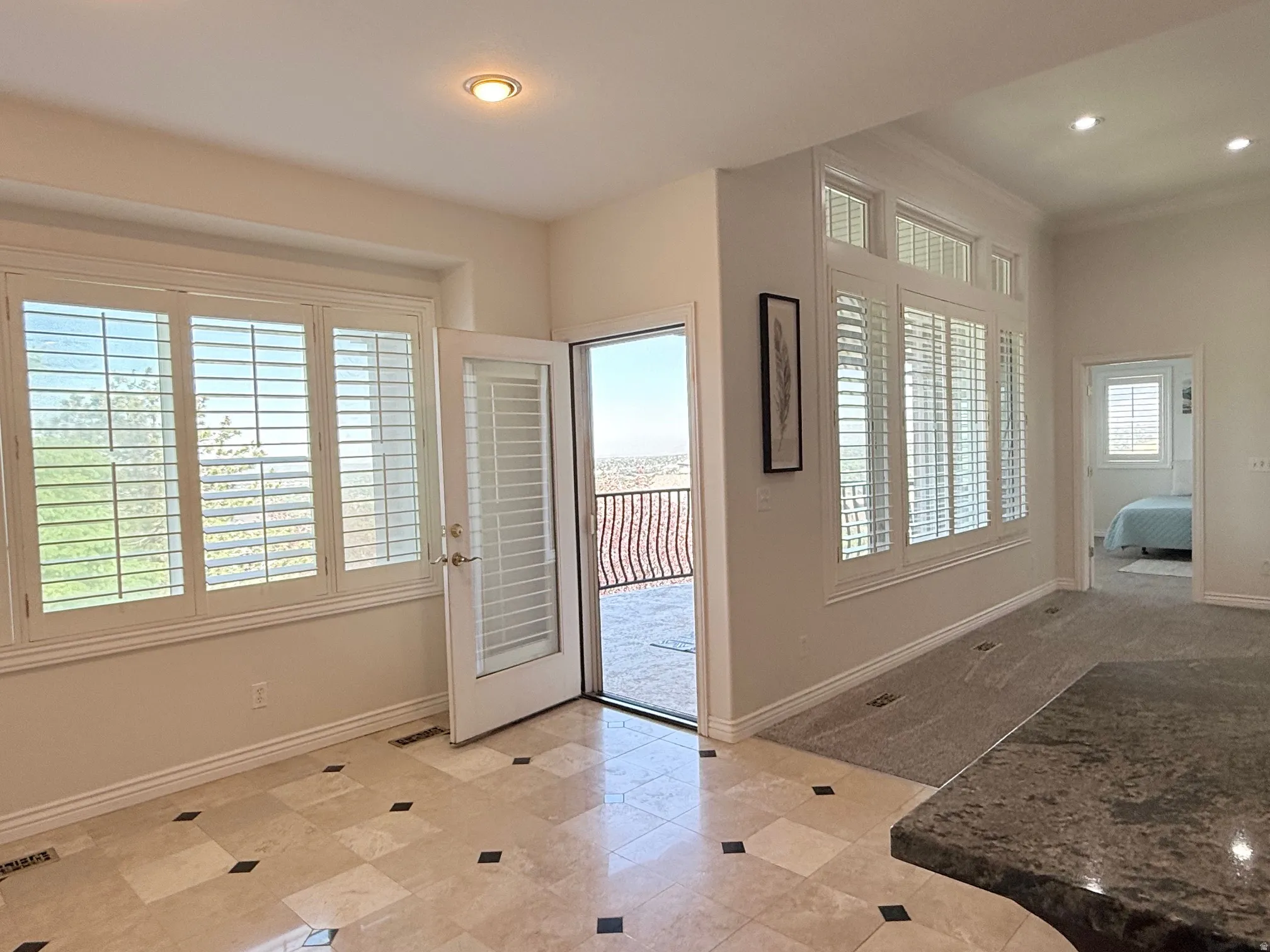 Tiled flooring featuring black accent squares, white plantation shutters, and a glass-paneled door opening to an exterior balcony with wrought iron railing