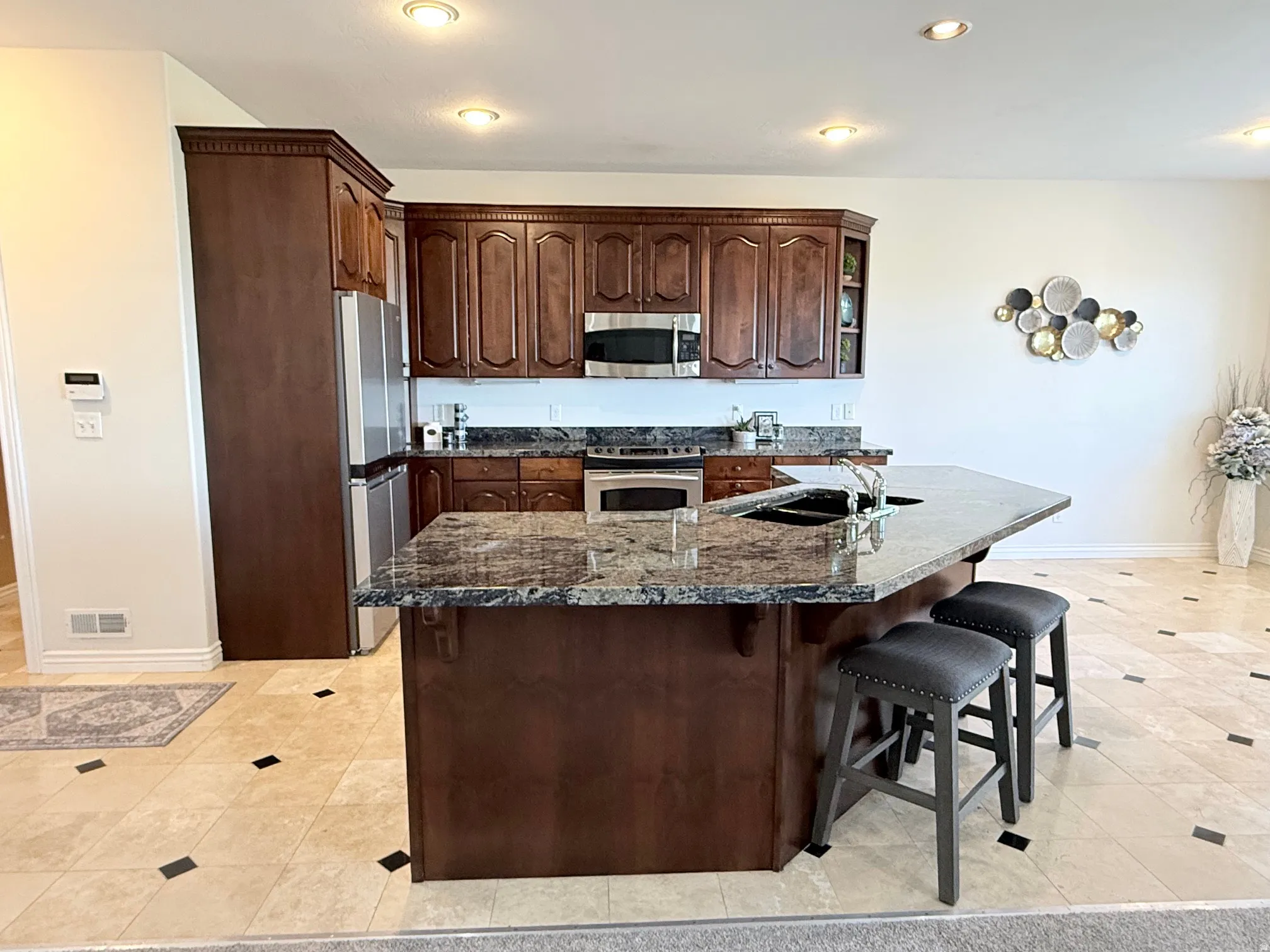 Kitchen featuring an expansive island with a dark granite countertop, a double basin sink, and integrated seating