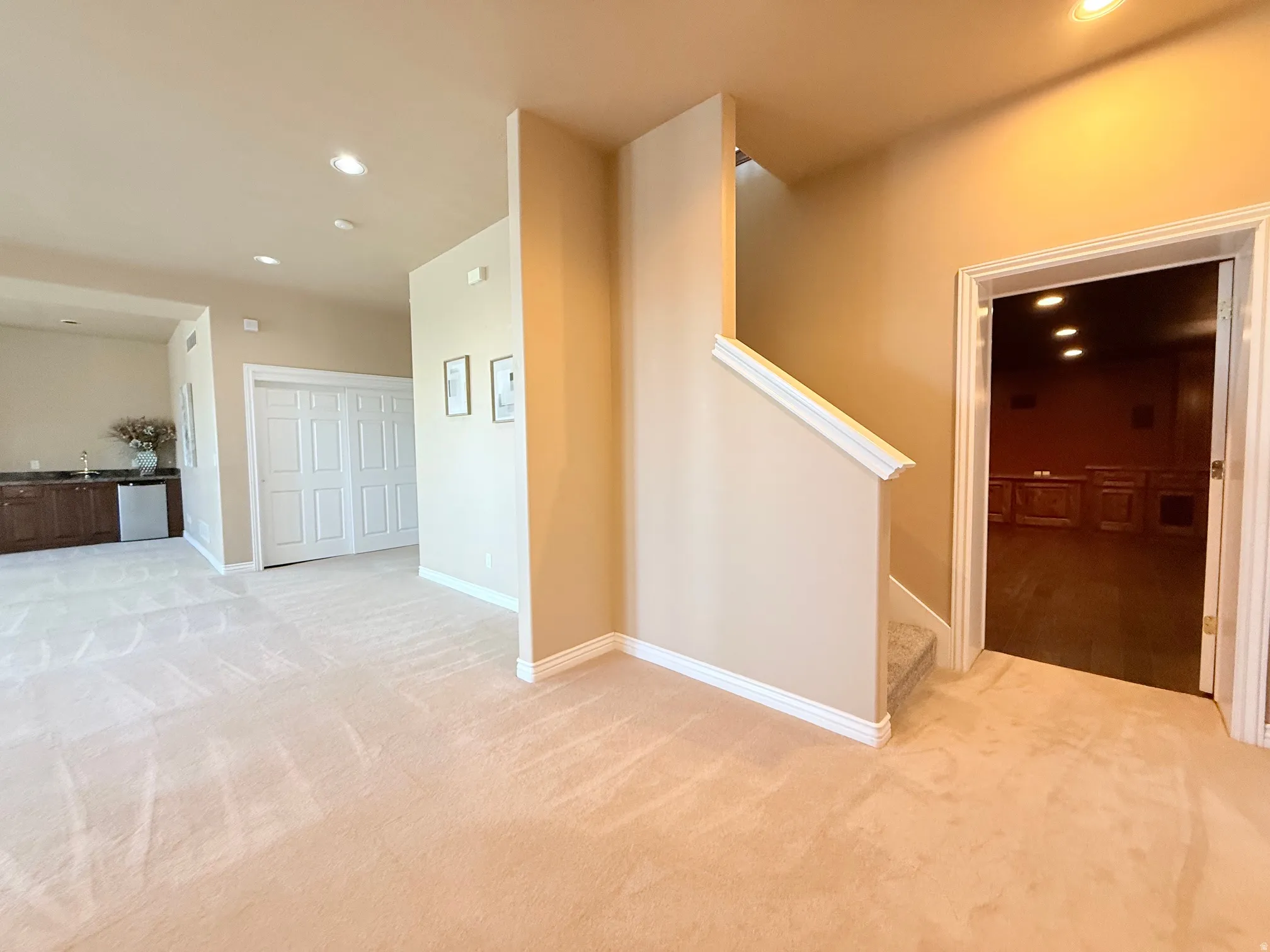Expansive carpeted area featuring a wet bar with dark wood cabinetry and a stainless steel under-counter refrigerator