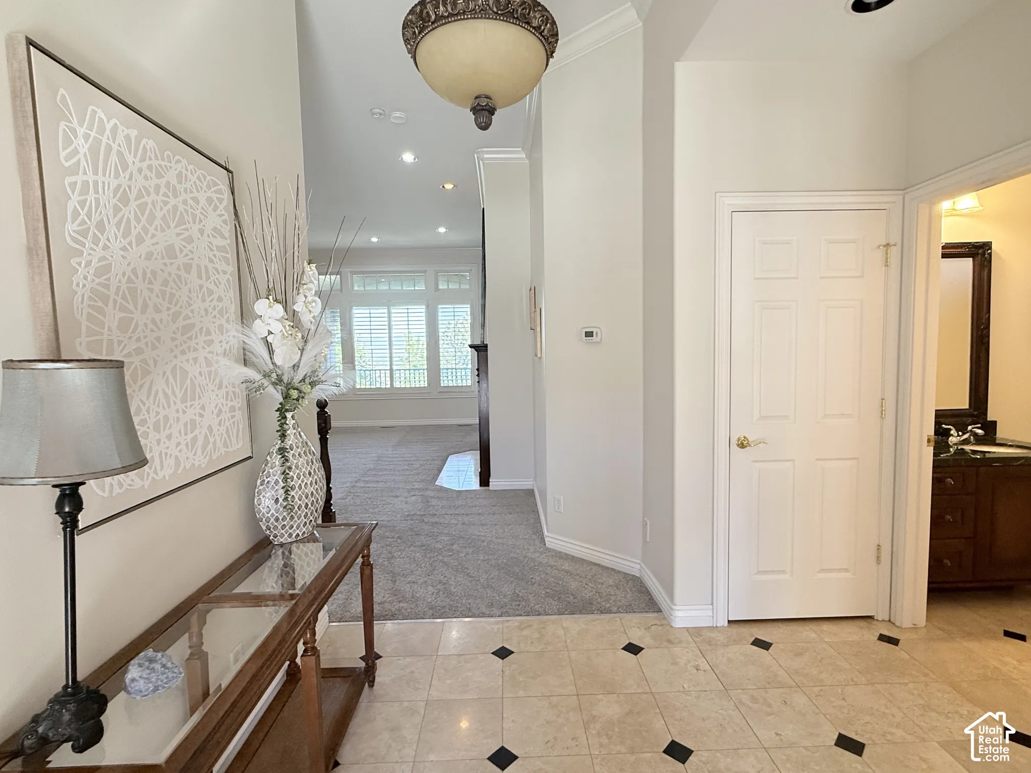 Entryway featuring light-toned tile flooring with dark accent squares, a decorative overhead light fixture, and crown molding