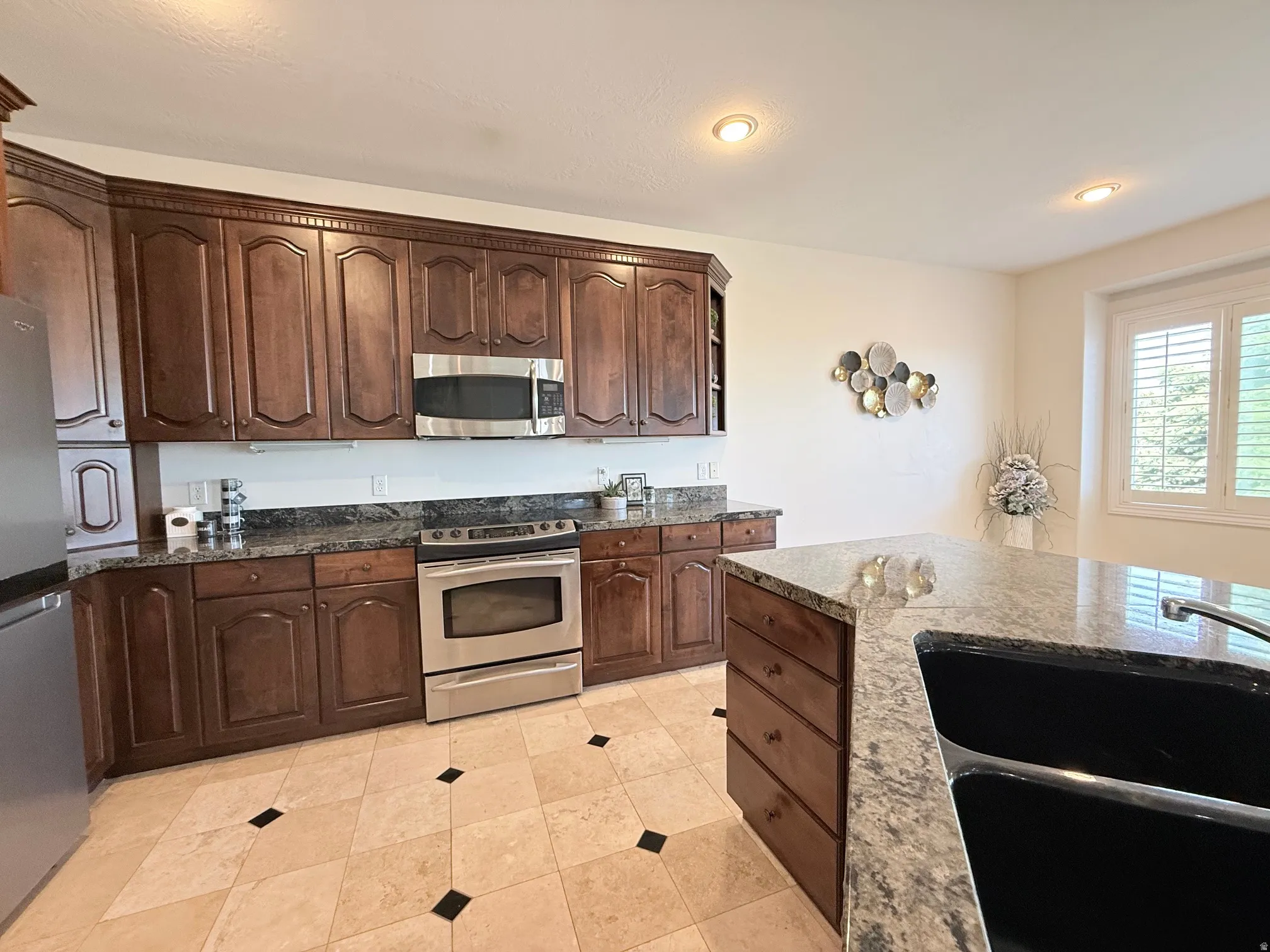 Kitchen featuring dark wood cabinetry, stainless steel appliances, speckled stone countertops, and a stone tile floor with black accents