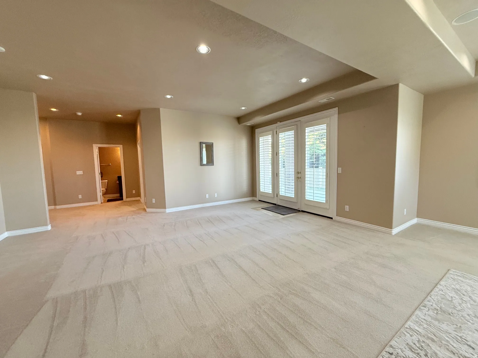 Spacious room featuring neutral carpeting, recessed ceiling lighting, and a tray ceiling detail