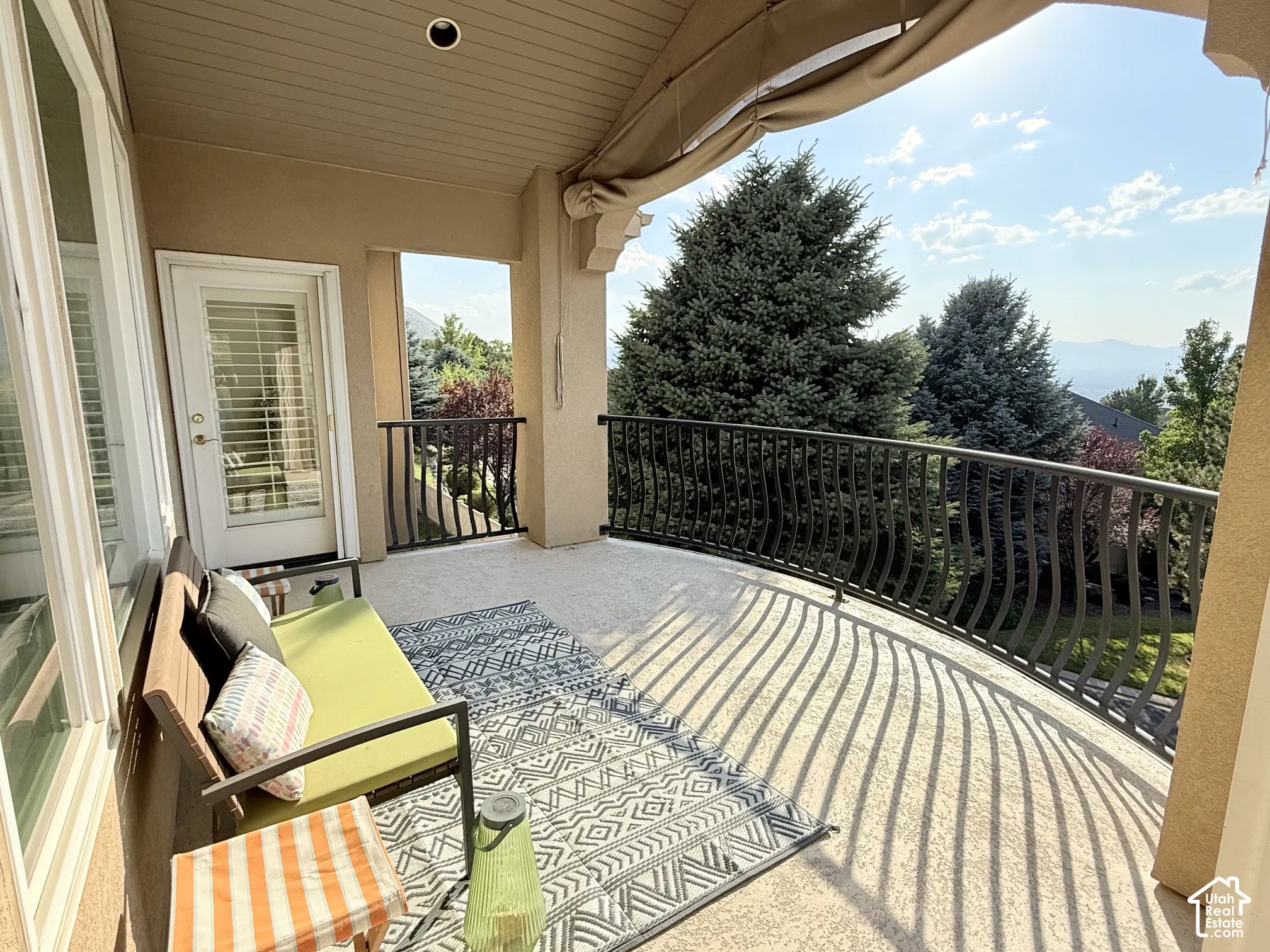 Spacious covered balcony featuring a wrought-iron railing, textured concrete flooring, and a recessed ceiling light