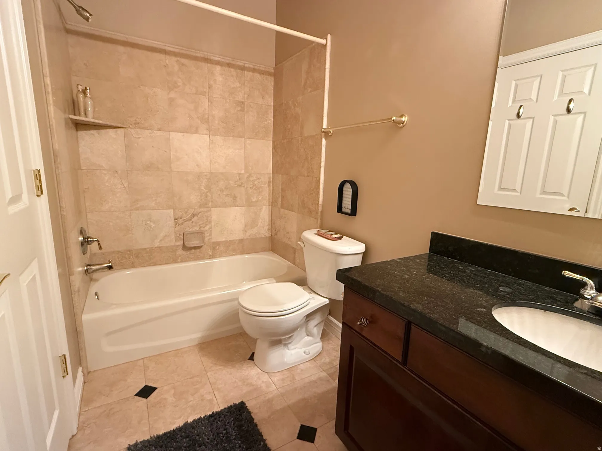Bathroom featuring a tiled shower surround, integrated bathtub, and a dark wood vanity with a stone countertop and undermount sink