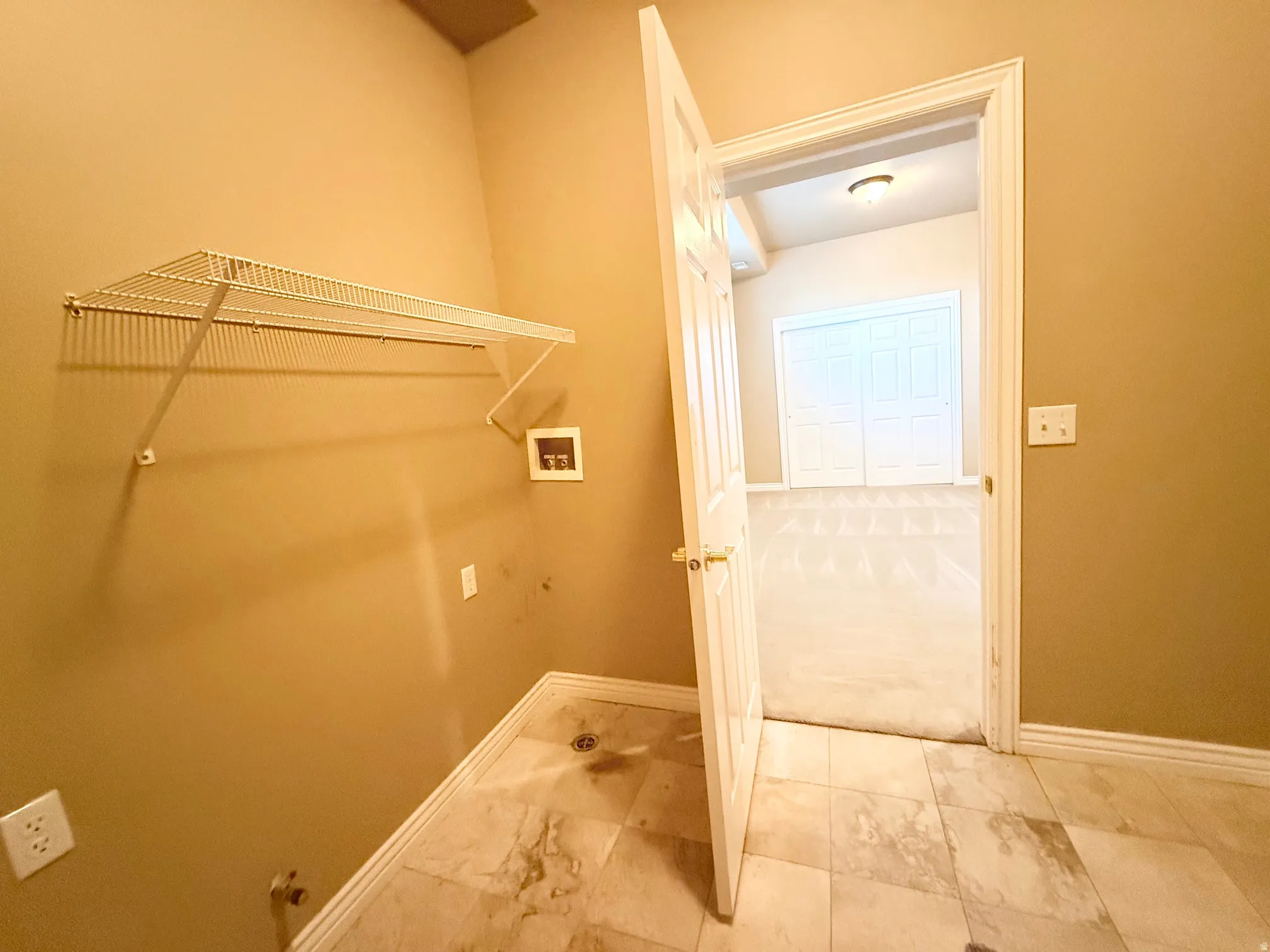 Utility area featuring tile flooring, a wall-mounted wire shelf, and washer/dryer hookups