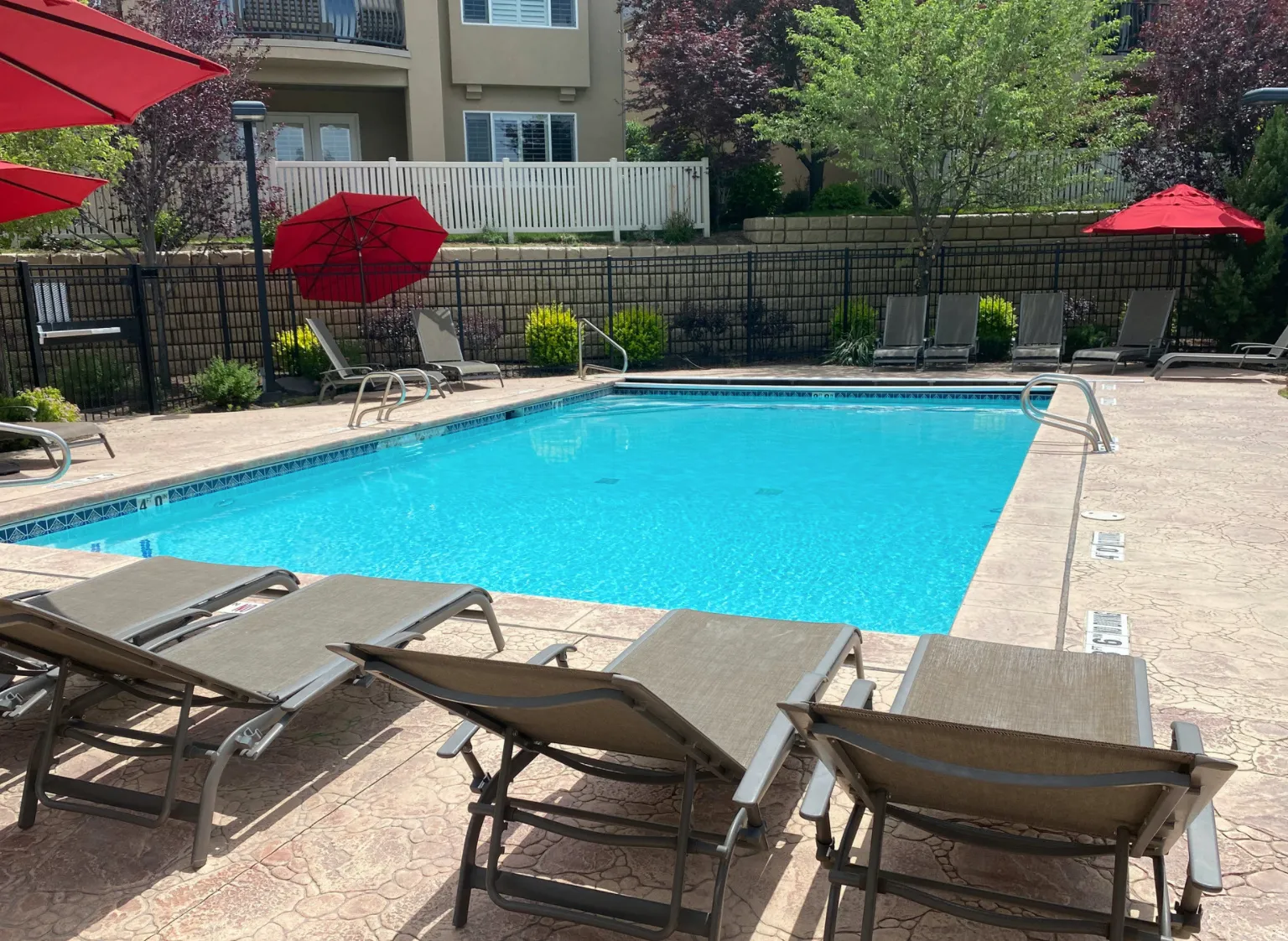 Refreshing swimming pool featuring a patterned concrete deck, perimeter fencing, and mature landscaping