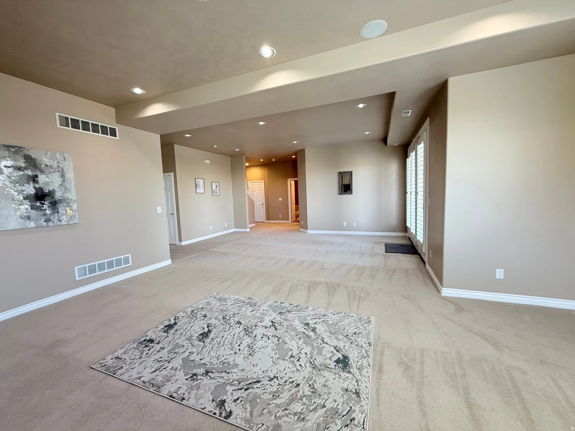 Spacious interior room with neutral-toned walls, recessed lighting, and light-colored carpet flooring