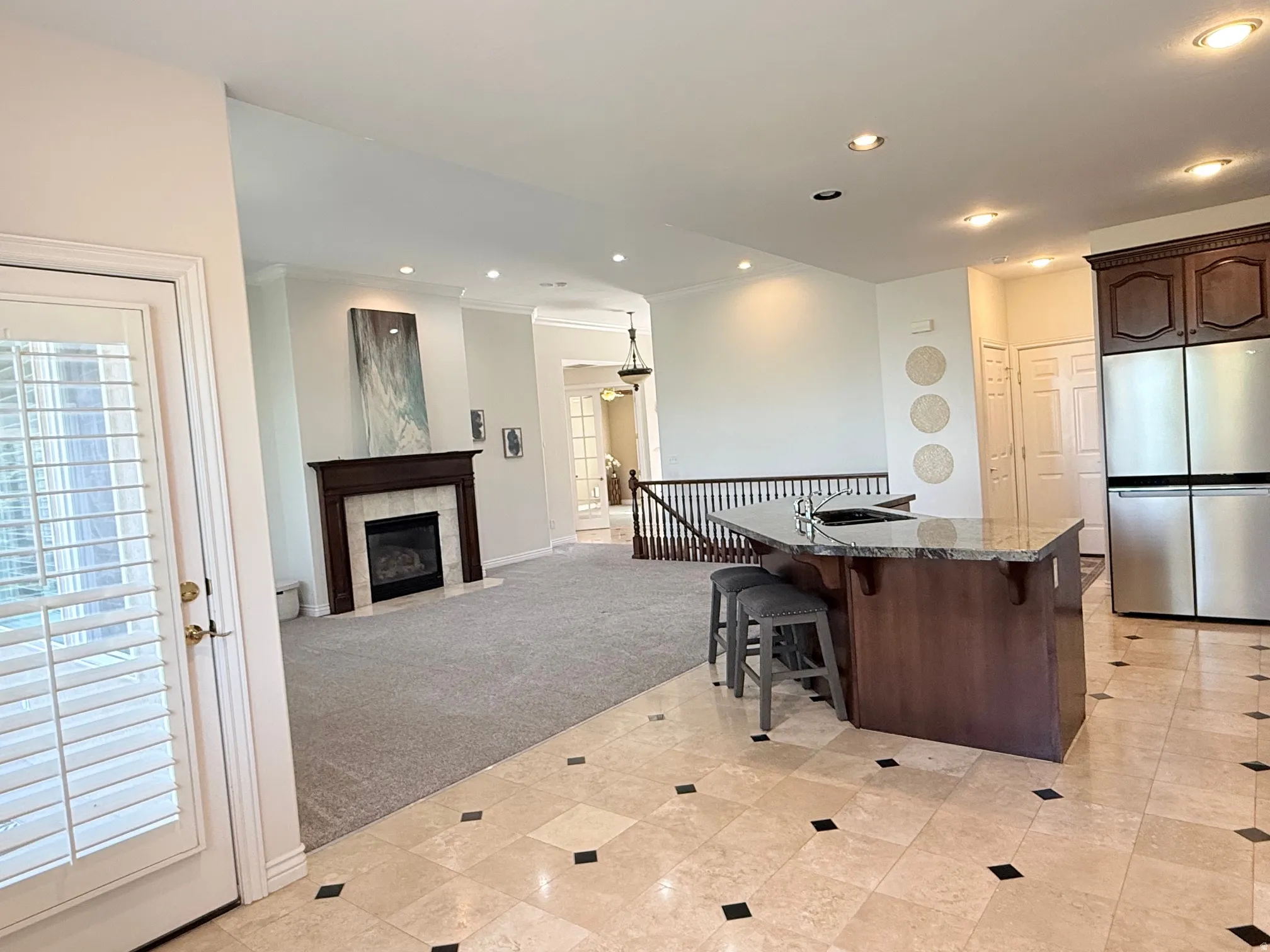 Open-concept living space featuring a fireplace with a wood mantle, recessed lighting, and a kitchen island with a stone countertop and built-in sink