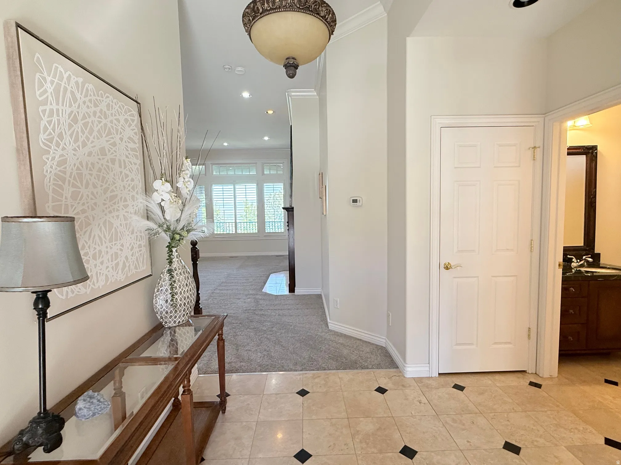 Entryway featuring light-toned tile flooring with dark accent squares, a decorative overhead light fixture, and crown molding
