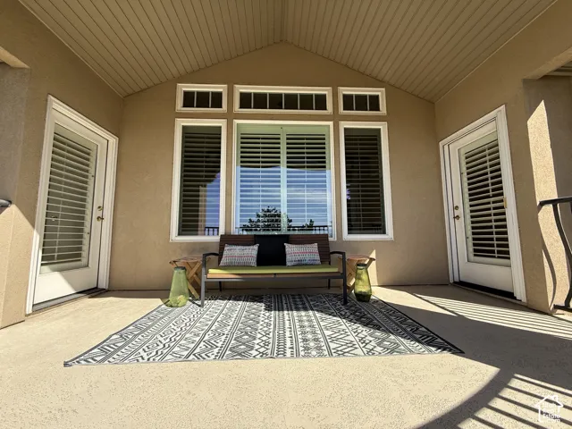 Covered patio featuring an angled wood-finish ceiling, textured exterior walls, multiple windows with plantation shutters, and two glass-paneled doors with internal blinds