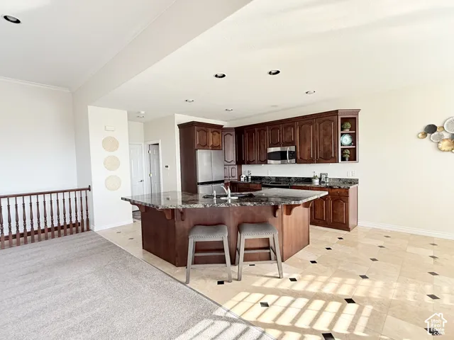 Open-concept kitchen featuring an island with stone countertop, rich wood cabinetry, and stainless steel appliances