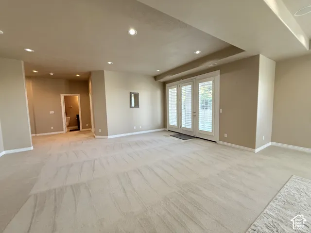 Spacious room featuring neutral carpeting, recessed ceiling lighting, and a tray ceiling detail