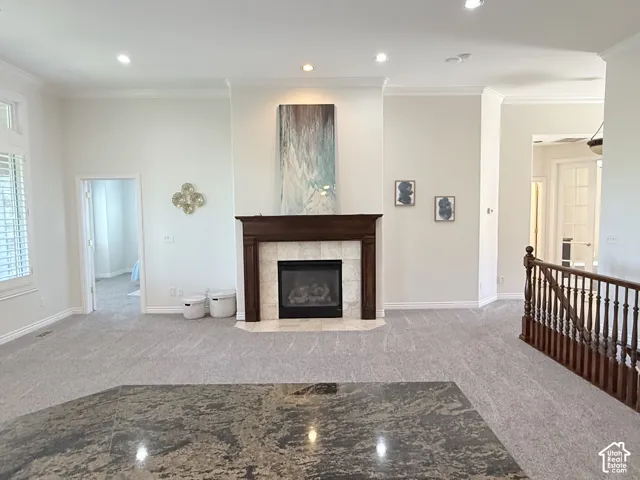 Living area featuring a traditional fireplace with wood mantel and tile surround, recessed lighting, crown molding, and light gray patterned carpet
