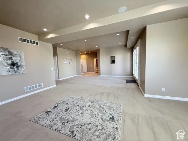 Spacious interior room with neutral-toned walls, recessed lighting, and light-colored carpet flooring