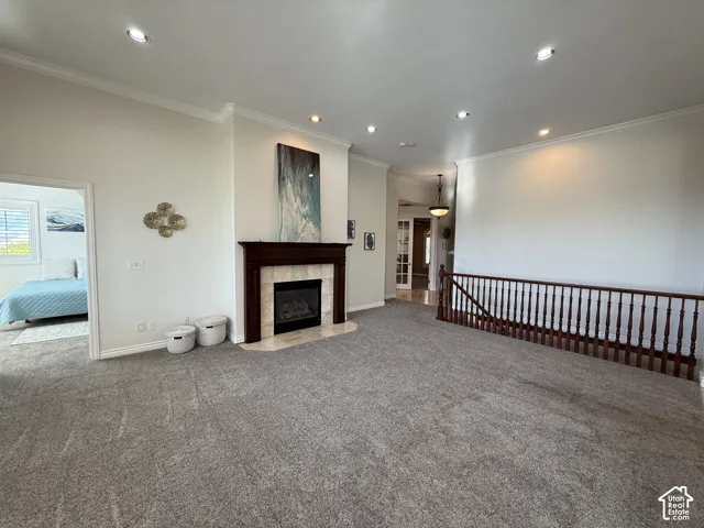 Living area featuring a dark wood mantel fireplace with a light tile surround, crown molding, recessed lighting, and grey carpet flooring