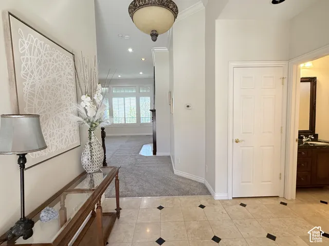 Entryway featuring light-toned tile flooring with dark accent squares, a decorative overhead light fixture, and crown molding