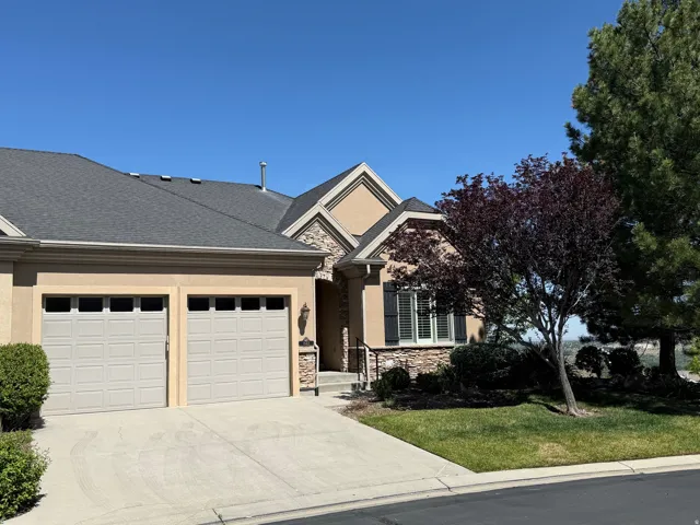 Stucco and stone exterior featuring a two-car garage, dark asphalt shingle roof, and a mature tree providing shade
