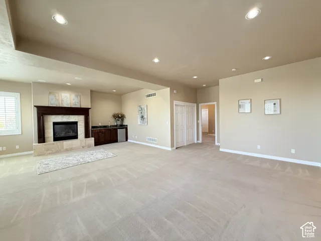 Spacious room featuring a fireplace with a wood mantle and stone surround, a built-in wet bar with cabinetry, recessed lighting, and neutral-toned carpeting
