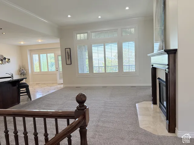 Open-concept living space with light gray carpeting, a dark wood-finish fireplace surround with a tiled hearth, and large windows featuring plantation shutters