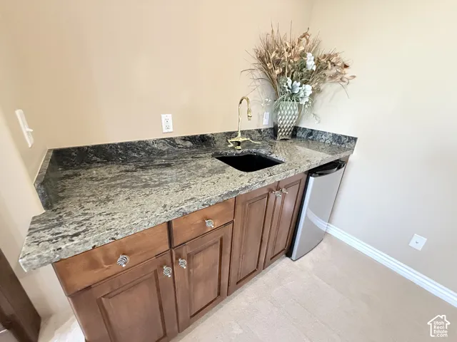Wet bar featuring a dark granite countertop with a polished finish, undermount sink, and a brass faucet