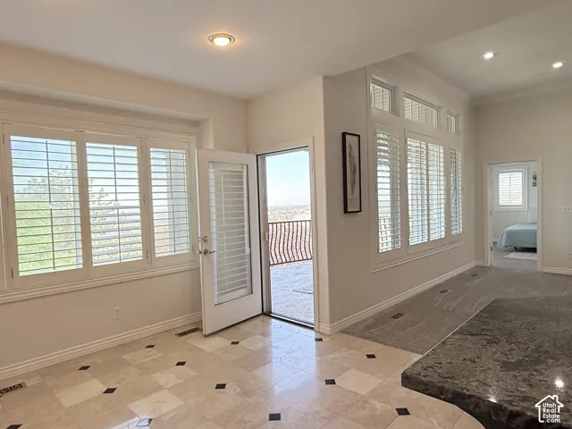 Tiled flooring featuring black accent squares, white plantation shutters, and a glass-paneled door opening to an exterior balcony with wrought iron railing