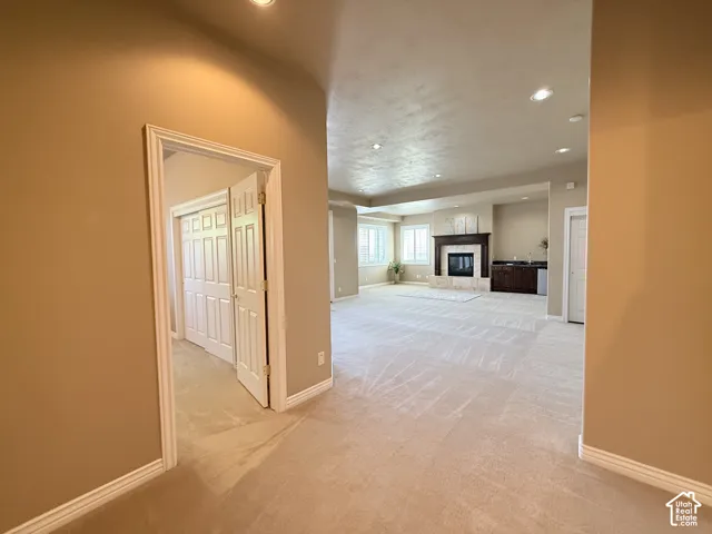 Spacious room with plush carpeting, recessed lighting, and a prominent fireplace featuring a dark wood mantel and light-toned stone surround
