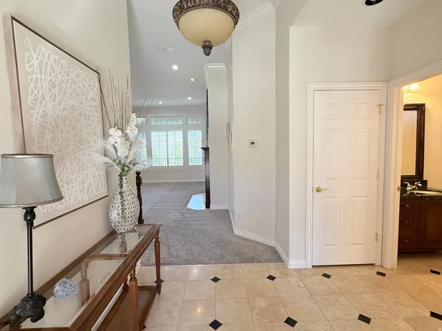 Entryway featuring light-toned tile flooring with dark accent squares, a decorative overhead light fixture, and crown molding