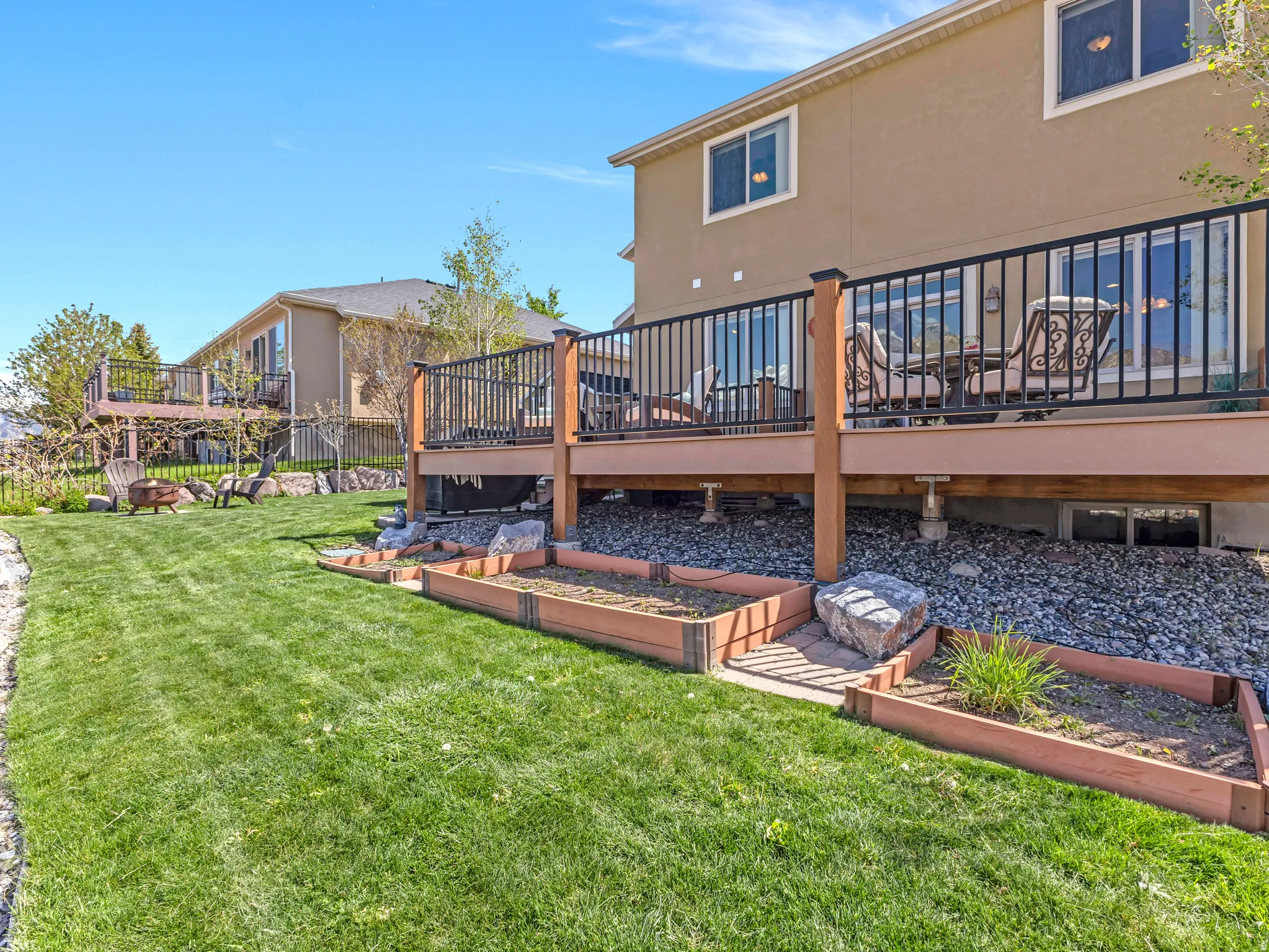 Spacious backyard featuring a manicured lawn, a multi-level deck with black railings, and tiered raised garden beds