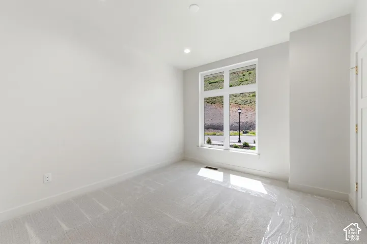 Carpeted interior space featuring a large multi-pane window, white walls, recessed ceiling lighting, and white baseboards