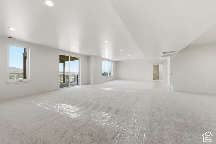Expansive lower-level space featuring light-toned carpeting, recessed ceiling lighting, multiple windows, and a sliding glass door providing exterior access