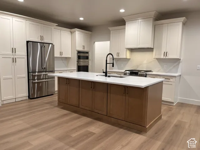 Kitchen featuring white shaker-style cabinetry, wood-finish center island, quartz countertops, stainless steel double wall ovens and refrigerator, and wood-finish flooring
