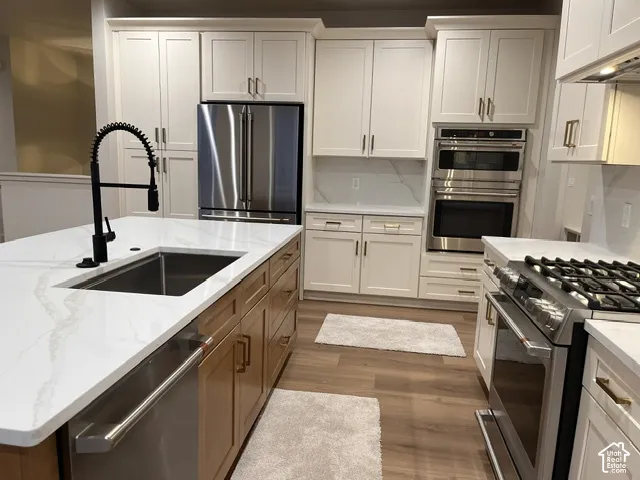 Kitchen featuring a large center island with a stone countertop, white cabinetry with gold-tone hardware, stainless steel wall-mounted double ovens, gas range, and wood-finish flooring